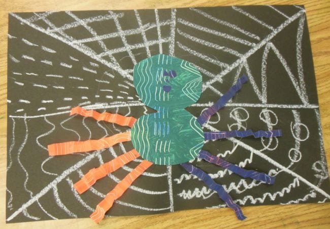 Chalk spiderweb drawn on black construction paper, with patterned paper spider on top (First Grade Art)