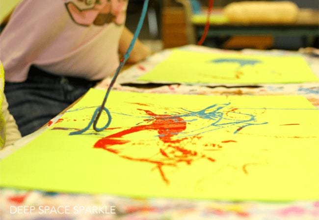 First grade art student pulling paint-covered yarn along a piece of paper