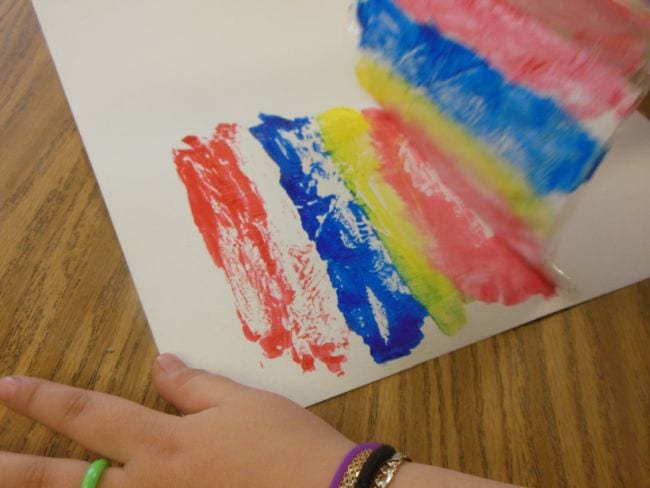 Student using a plastic bag to print paint stripes on a piece of paper