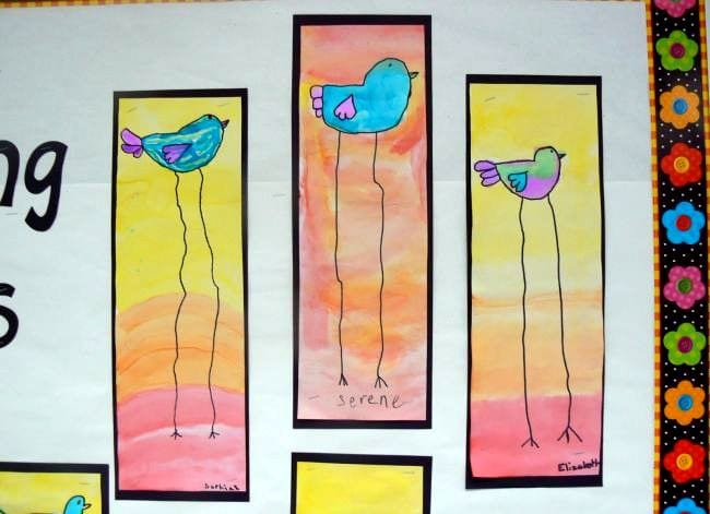 Long-legged blue birds on a watercolor background of yellow, orange, and pink