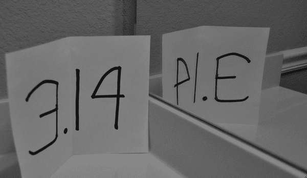 Carte d'index avec 3,14 écrit au marqueur noir posée à côté du miroir et montrant le reflet comme PIE