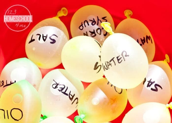 Water balloons in a large red bucket, labeled water, salt, corn syrup, oil, and more