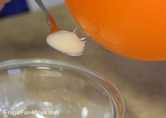 Orange balloon next to a spoon of white liquid being drawn to the balloon by static electricity