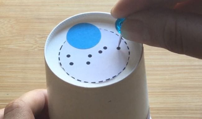 Estudiante de ciencias de tercer grado que hace agujeros en el fondo de un vaso de papel con la forma de una constelación