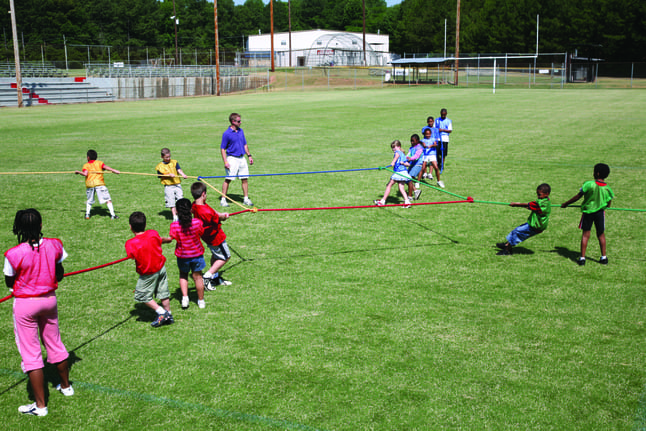 Students playing four way tug of war on a grassy field, as an example of team-building games and activities
