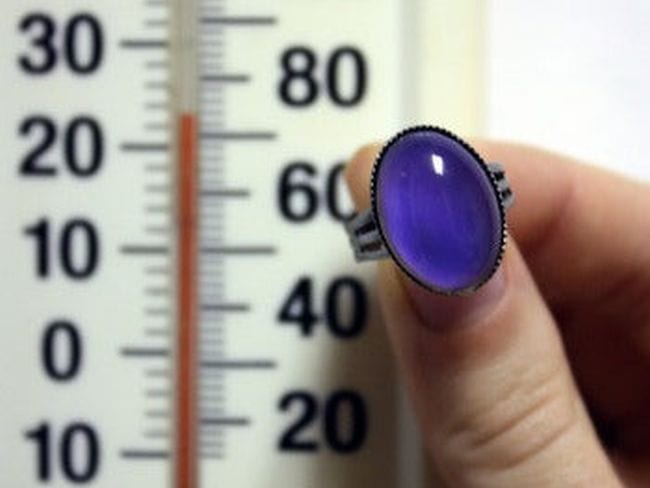 La mano de un estudiante sosteniendo un anillo del estado de ánimo azul frente a un termómetro