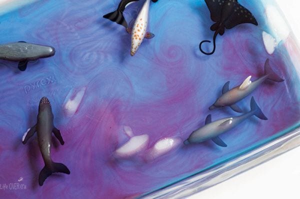 Glass pan full of blue and purple swirls of water, with ice cubes and plastic sea creatures