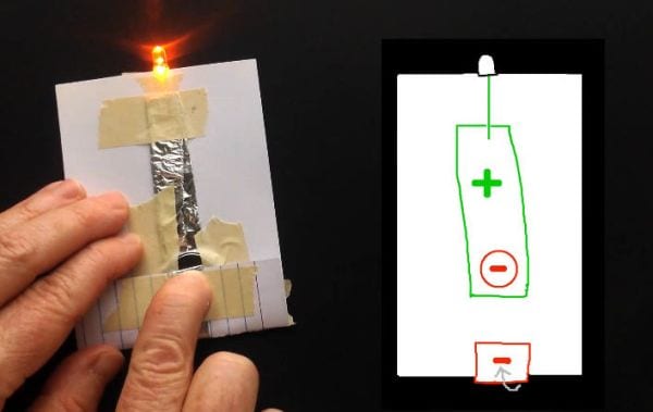 Student's hand powering a flashlight made from index card, LED, foil, and masking tape's hand powering a flashlight made from index card, LED, foil, and masking tape