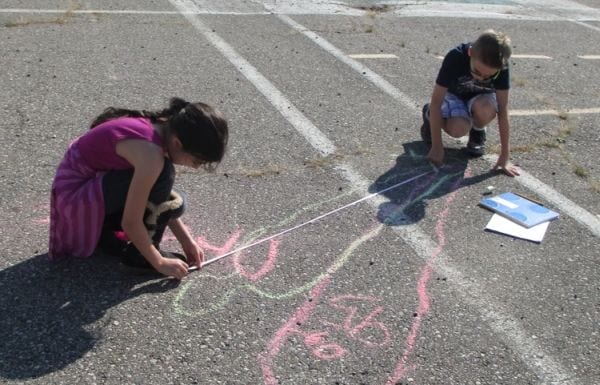 Los alumnos de ciencias de cuarto grado miden sus contornos dibujados con tiza de acera en el patio