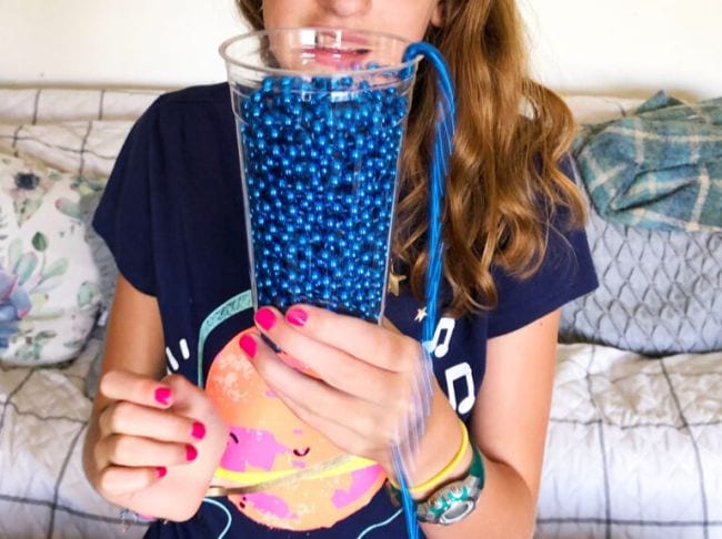 Child holding a cup of blue bead strings, watching them flow out of the cup