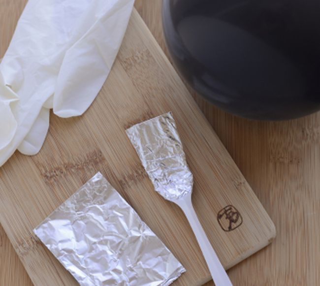 Foil covered plastic fork with piece of foil and rubber glove on a wood board