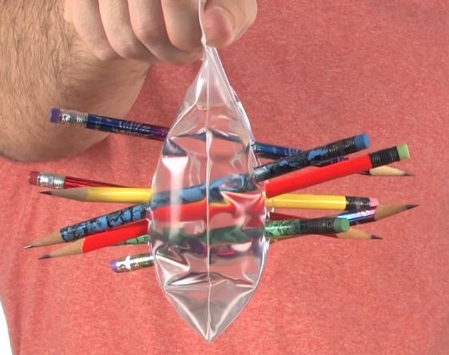 Man holding a zip top bag filled with water, with multiple pencils stuck through the bag