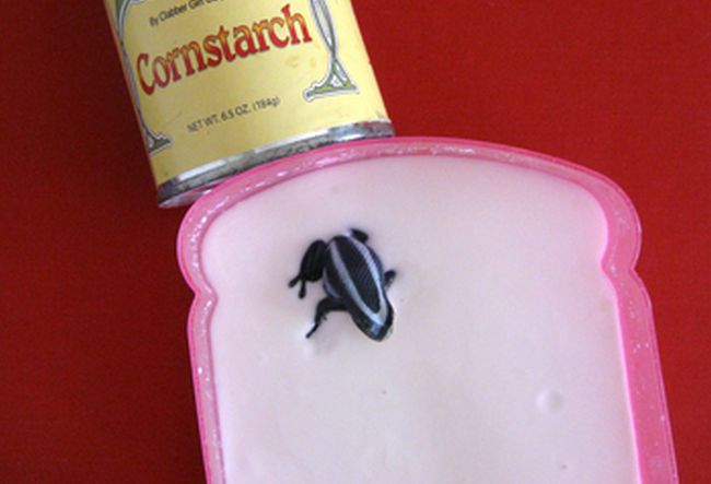 Can of cornstarch next to a dish filled with a white liquid cornstarch mixture with a small plastic frog on top