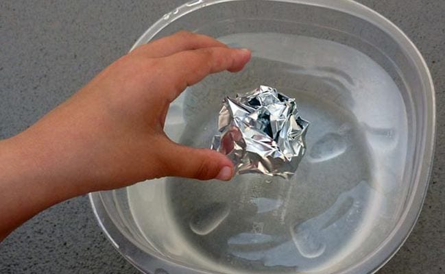 Sixth grade science student dropping a ball of aluminum foil into a plastic container of water
