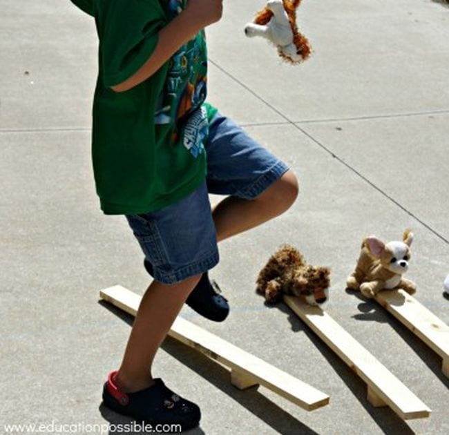 Sixth grade science student stomping on a basic catapult made from a wood block and piece of lumber, sending stuffed animals flying