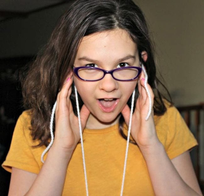 Sixth grade science student holding yarn strings to her ears and looking surprised