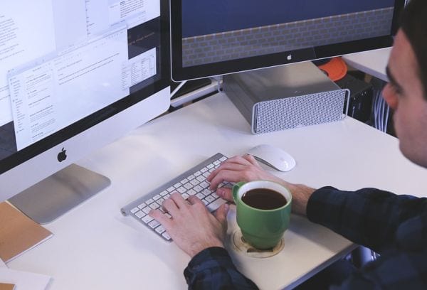 Man typing at a computer with a cup of coffee in front of him