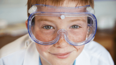 close up of boy wearing lab coat and goggles