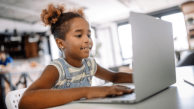 Elementary school girl on laptop, smiling.