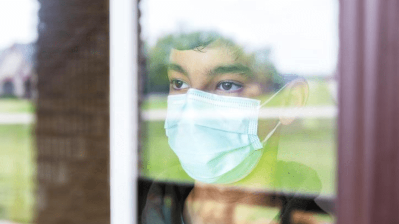 sad teen boy wearing mask gazing out window - youth suicide prevention