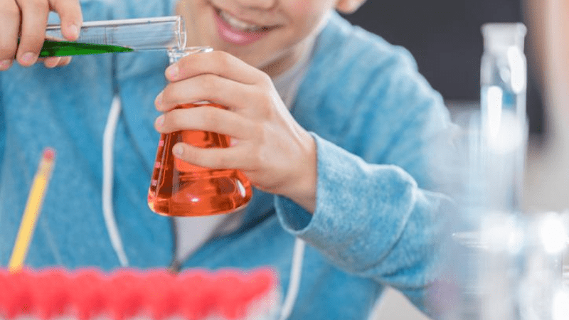boy pouring colored liquid into beaker - lab safety at home