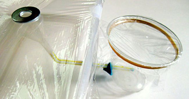 Plastic wrap covered container of water linked to a cup by drinking straw