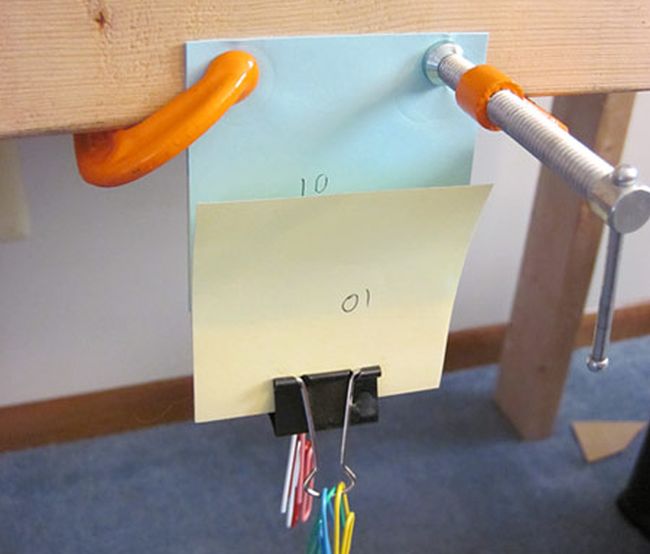 Orange clamps holding sticky notes to a piece of wood, with a binder clip at the bottom holding paper clips (Eighth Grade Science)