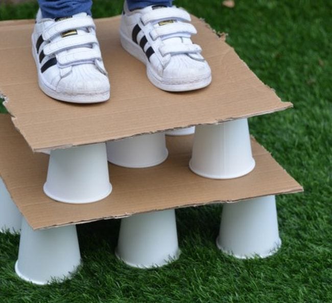 Child standing on a stack of paper cups and cardboard squares