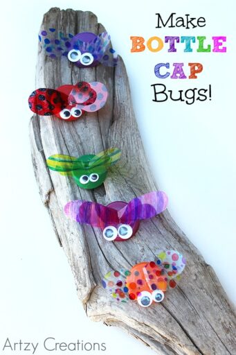 colorful bugs made from bottle caps sitting on a piece of driftwood