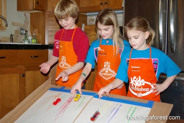 Three students using matchbox cars dipped in paint to draw on a sheet of paper (NASCAR Teaching Ideas)