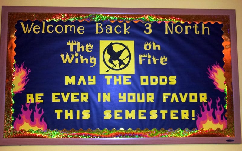 Hunger Games themed bulletin board welcoming kids back to school. Text reads "Welcome Back 3 North, the Wing on Fire. May the odds be ever in your favor this semester!"