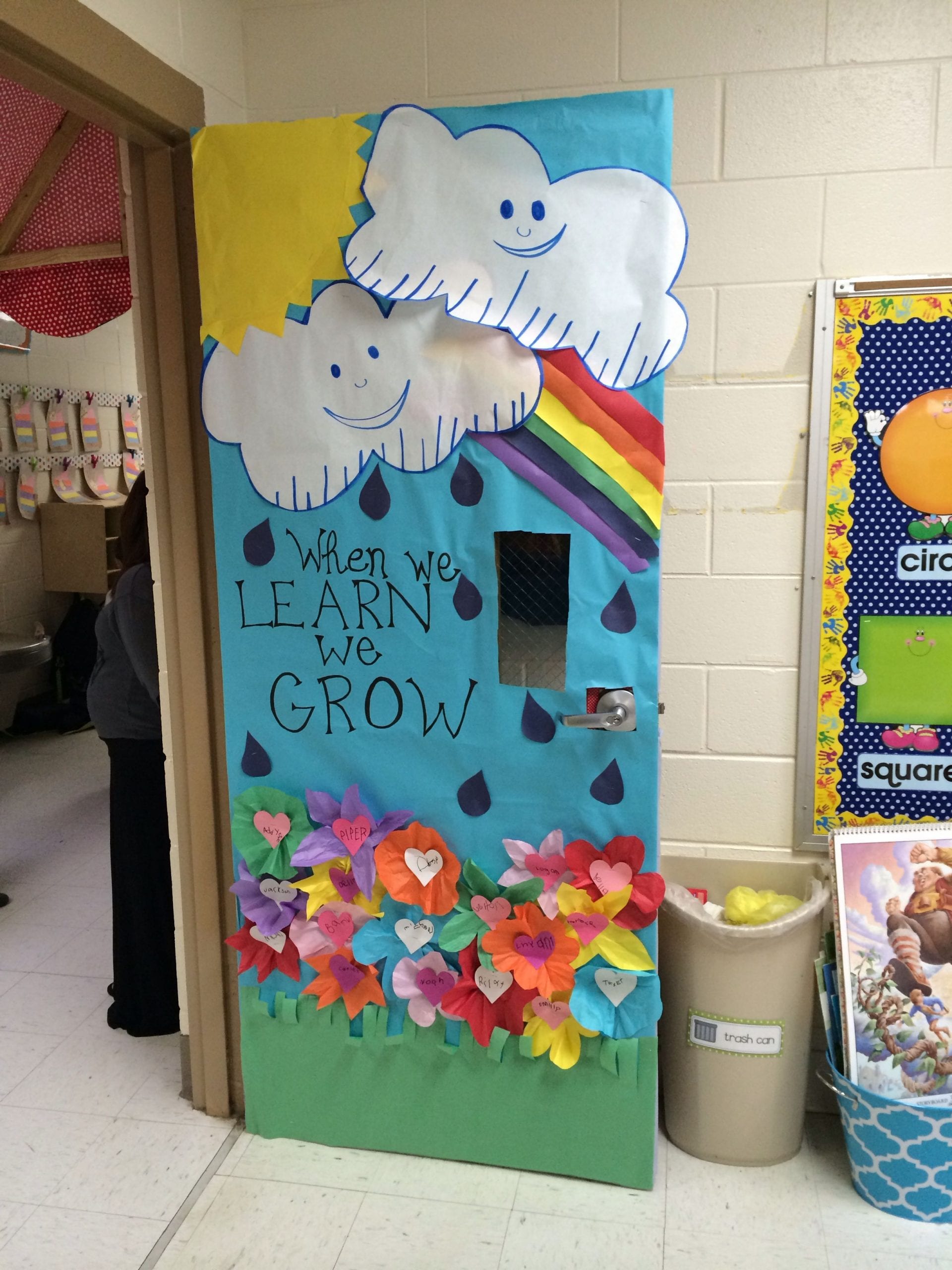 Door decoration with smiling clouds raining onto flowers, with the text "When we Learn we Grow"