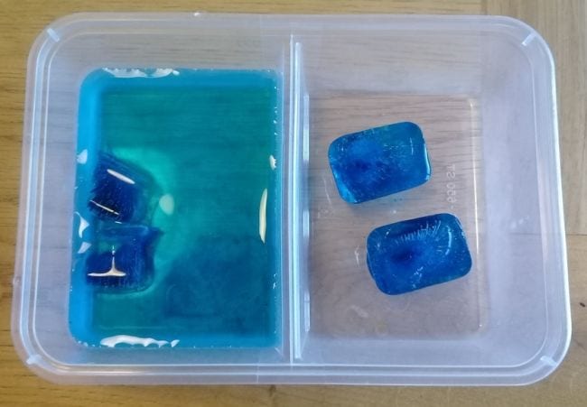 Голубые кубики льда в разделенном контейнере, левая сторона которого также содержит воду (Деятельность по изменению климата)