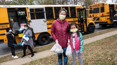 Asian American woman and daughter standing in front of school bus free meals for kids