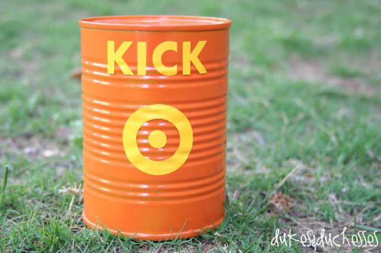 A tin can is spray painted orange with the word KICK in yellow as well as a yellow bulls eye on it.