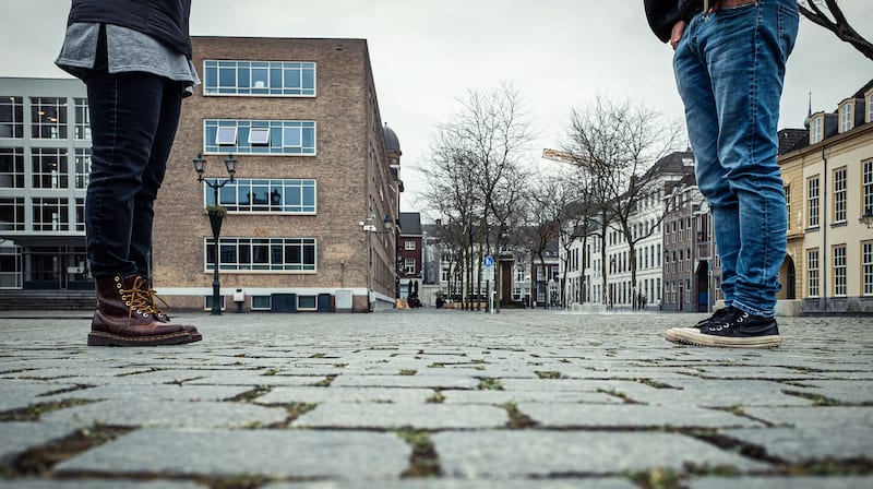 Two students social distancing. The image contains only the students lego with buildings in the background.