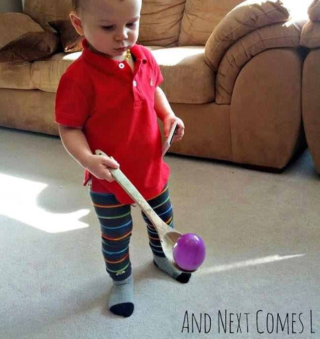 Toddler carrying a plastic egg on a wooden spoon