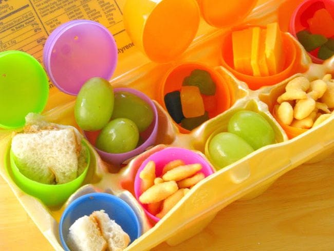 Plastic eggs filled with small snacks like grapes and goldfish crackers, set into a foam egg crate (Easter Egg Activities)