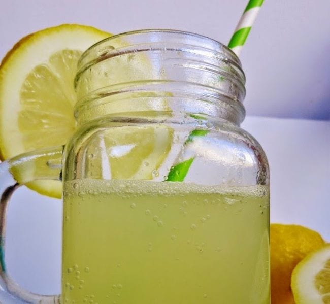Mason jar mug holding carbonated lemonade with lemon slice and green and white striped straw (Edible Science)