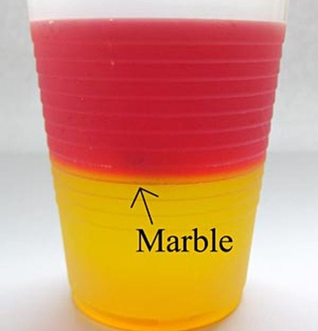 Layers of red and yellow jello in a plastic cup with marble indicated by an arrow