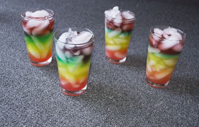 Four glasses containing rainbow layers of liquid with ice cubes (Edible Science)
