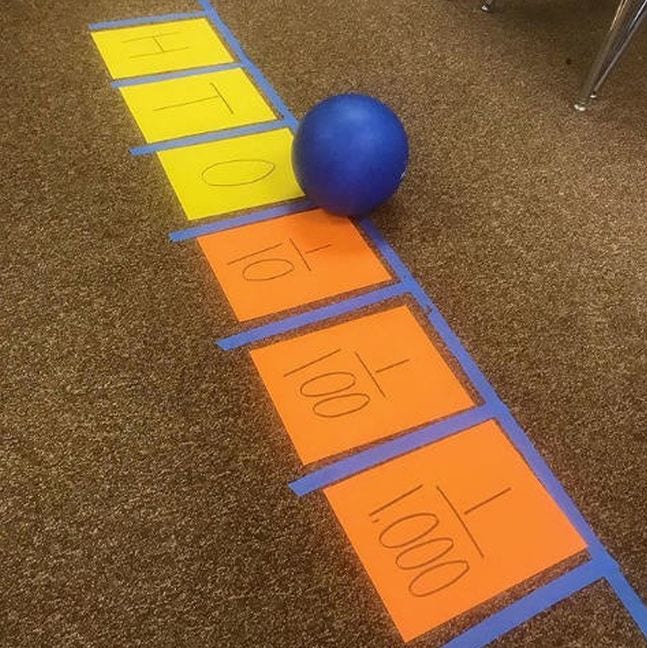 Taped number line on the floor with a blue ball used as a decimal