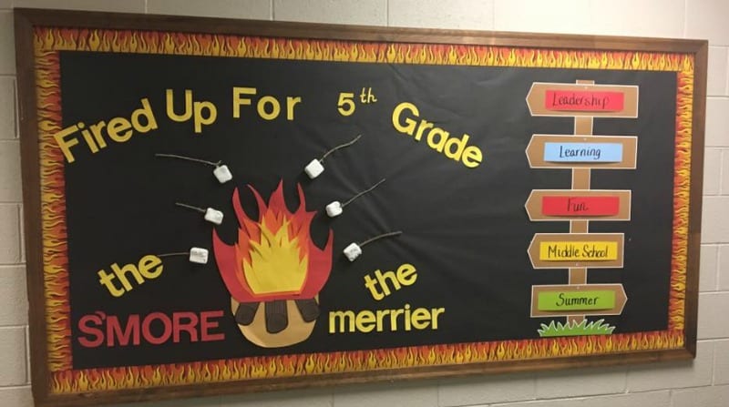 S'mores Bulletin Board that reads Fired Up for 5th Grade. The SMORE the merrier. Board also has a campfire and sign board.