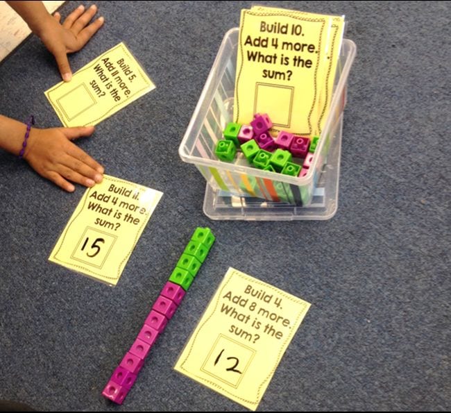 Math cubes with printed cards saying "Build 4. Add 8 more. What is the sum?"