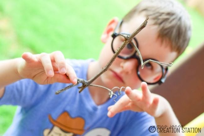 Child wearing toy glasses to examine a twig from a tree