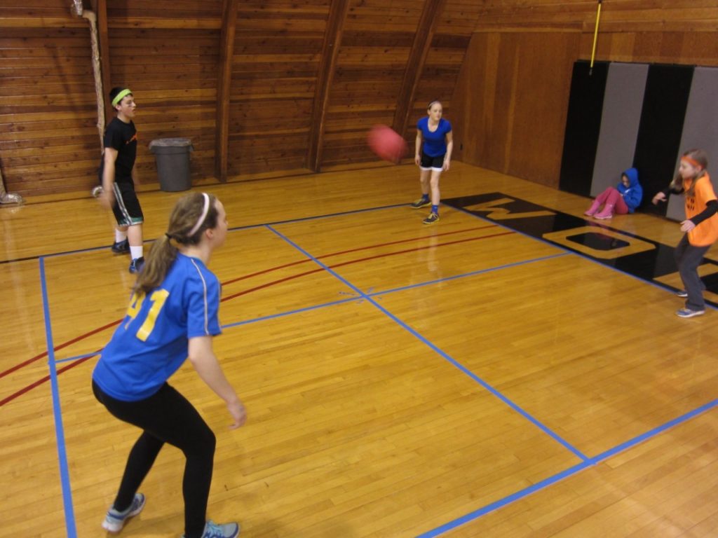 Four students stand on the four corners of a square. A ball is shown moving between them.