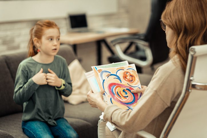 A woman and a little girl sit facing each other. The woman is holding several pieces of a child's artwork. (art careers)