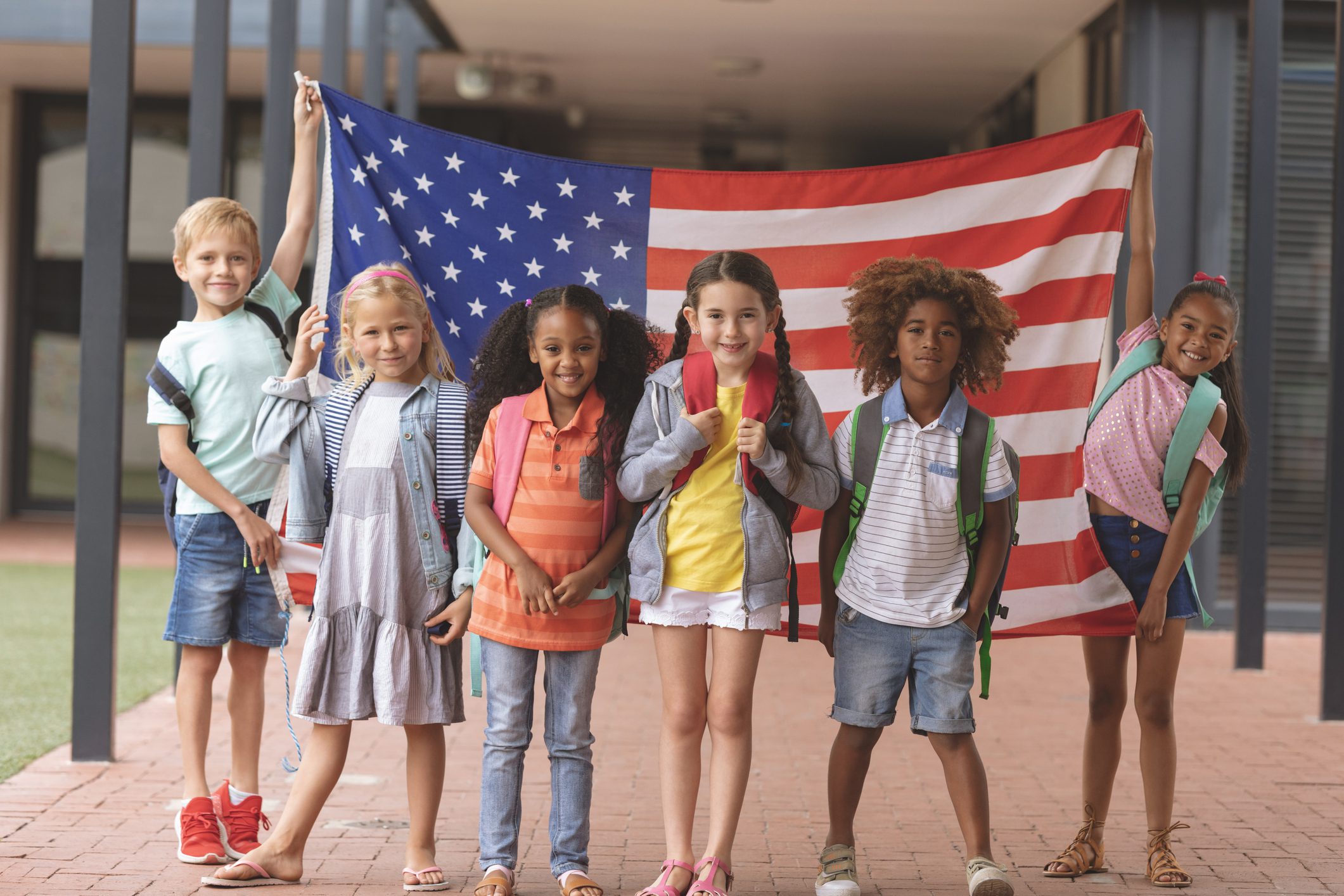 Happy school students standing in corridor while holding American flag