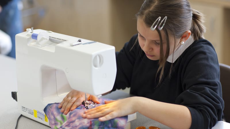 A female high school student using sewing machine in textiles class.