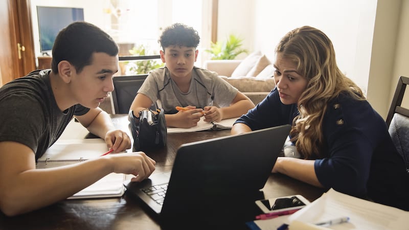 Hispanic mother with two teens looking at computer welcoming immigrant families at school